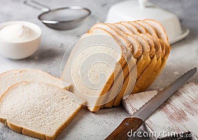 Cut of fresh loaf of white bread with flour and butter on light kitchen table background with chopping board and bread knife. Stock Photo