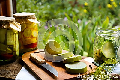 Cut fresh zucchini and jars of pickled vegetables on wooden table Stock Photo