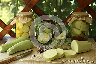 Cut fresh zucchini and jars of pickled vegetables on white wooden table Stock Photo