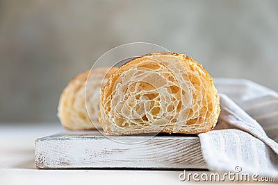 Cut in half croissant with inside texture and thin crisp layers on wooden board, light concrete background. Delicious french Stock Photo