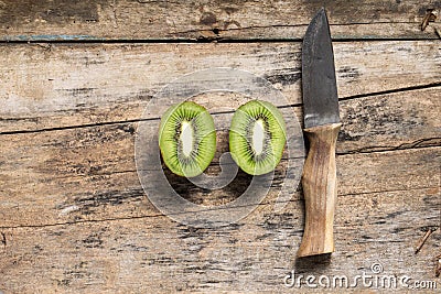 Cut in Half Kiwi with Knife lying on Textured Wooden Table. Top View Stock Photo