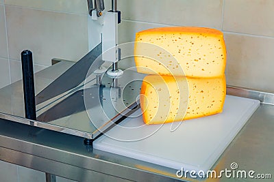 Cut head of cheese on an industrial cutter in a cheese factory. Stock Photo