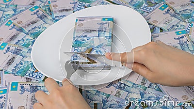 Cut off piece of money in a plate with a knife. Tenge, Kazakhstan. Concept, living wage. Economy, Central Asia. Sawing the budget Stock Photo