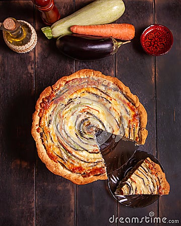 The cut piece of Vegetable Spiral tart with zucchini, eggplant, carrot on wooden background Stock Photo