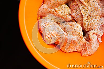 Cut pieces of uncooked chicken, seasoned with turmeric paste, inside plastic bowl Stock Photo