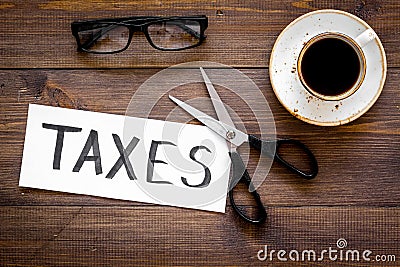 Cut taxes concept. Sciccors cut paper with word Taxes on dark wooden background top view Stock Photo