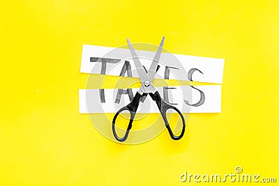 Cut taxes concept. Sciccors cut paper with word Taxes on yellow background top view space for text Stock Photo