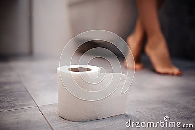 Cut view of rolled paper on floor. Young woman sit on toilet. Her feet in shot. Beautiful posed legs. Stock Photo