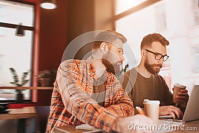 Cut view of two hipsters studying in cafe. One of them is working on computer while another one is lookint at what his Stock Photo