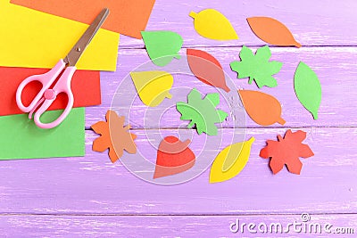 Cut yellow, green, red and orange paper leaves, scissors, colored paper sheets on lilac wooden background. Closeup Stock Photo