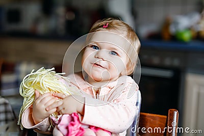 Cute adorable baby girl playing with first doll. Beautiful toddler child sitting in high chair at home. Happy healthy Stock Photo