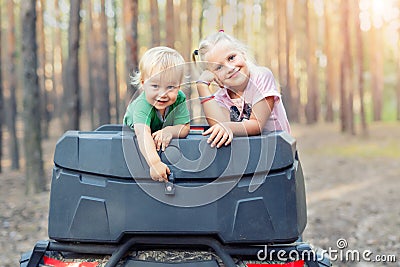 Cute adorable caucasian blond siblings having fun during atv 4x4 off-road adventure trip amog coniferous pine forest on brigh Stock Photo