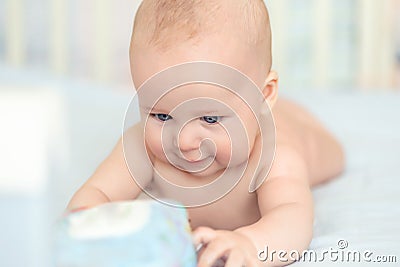 Cute adorable caucasian little 5 month old infant baby boy lying on tummy at nursery bed room having fun playing and Stock Photo