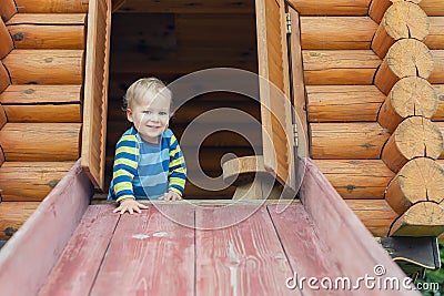 Cute adorable caucasian toddler boy having fun sliding down wooden slide at eco-friendly natural playground at backyard in autumn Stock Photo