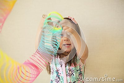 Cute adorable little girl playing with plastic rainbow magic spring, holding bouncy stretchy toy and smiling at camera Editorial Stock Photo