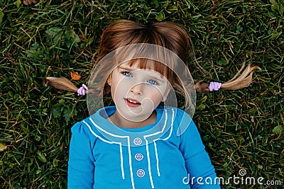 cute adorable little red-haired Caucasian girl child in blue dress lying in field meadow park outside Stock Photo