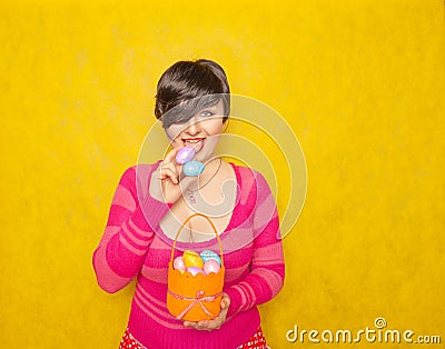 Pretty adult chubby woman with short hair holding colorful holiday eggs and a easter basket on yellow solid studio background Stock Photo