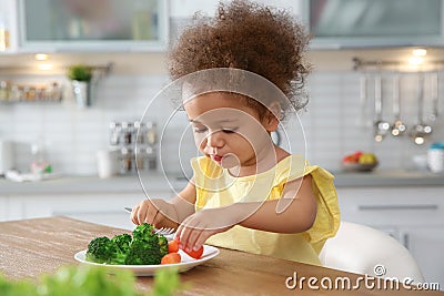 Cute African-American girl eating vegetables at table Stock Photo