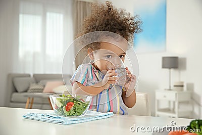 Cute African-American girl with glass of water and vegetable salad at table Stock Photo