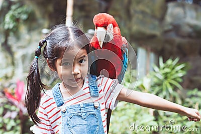 Cute asian child girl with macaw parrot in her shoulder Stock Photo