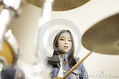 A cute Asian elementary school girl playing a drum in a music classroom Stock Photo
