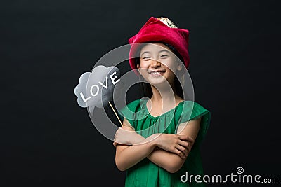 cute asian girl child dressed in a green dress holding a Christmas hat and a love stick on a black background Stock Photo