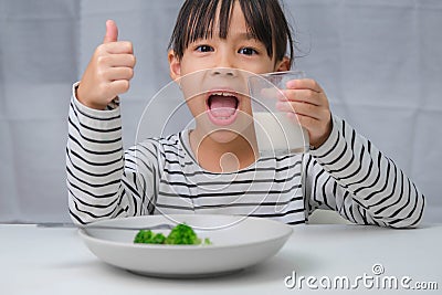 Cute Asian girl drinking a glass of milk in the morning before going to school. Little girl eats healthy vegetables and milk for Stock Photo