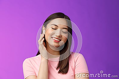 Cute asian girl enjoying listening music, put on wireless headphone, tilt head close eyes dreamy smiling satisfaction Stock Photo