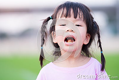 Cute Asian girl has dry and peeling lips. Children eat vitamin C orange color. Child opened his mouth wide. Kid braided two braids Stock Photo