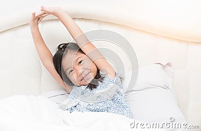 Cute asian girl in pajamas is sitting on bed stretching. Stock Photo