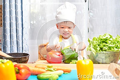 Cute Asian little boy child wearing chef hat and apron having fun preparing, cooking healthy food in kitchen, Fun indoor Stock Photo