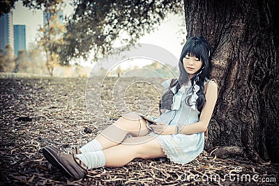 A cute Asian Thai girl is leaning on a tree trunk sleeping while Stock Photo