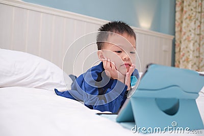 Cute Asian toddler boy child lying on his stomach while playing game, watching cartoon, using tablet pc computer, Gadget addicted Stock Photo