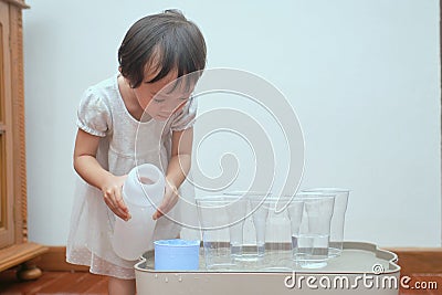 Cute Asian toddler girl having fun playing with water table at home, Wet Pouring Montessori Preschool Practical Life Activities, Stock Photo
