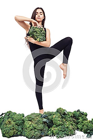 Cute athletic girl holds large head of fresh broccoli in front of her and practices yoga Stock Photo