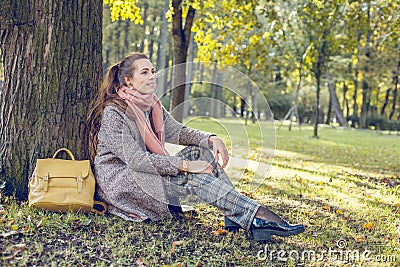 Cute autumn woman sitting near tree outdoors. Romantic girl in fall park Stock Photo