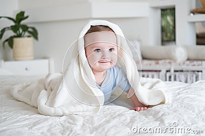 Cute baby boy 6 months old in blu bodysuit smiling and lying on bed with white plaid at home Stock Photo