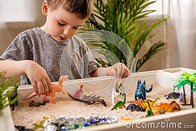 Cute baby boy playing sensory box kinetic sand table with carnivorous and herbivorous dinosaurs Stock Photo