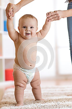 Cute baby boy taking first steps holding mother hands Stock Photo