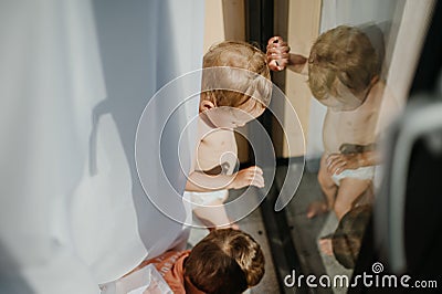 Cute baby girl and boy playing,hiding behind curtains at home. Stock Photo