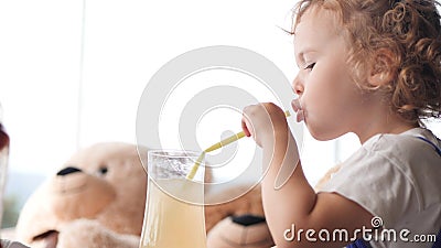 Cute baby girl drinks lemonade with in a cafe with many teddy bears Stock Photo