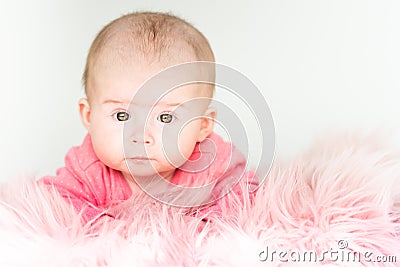 Cute baby girl lying on furry blanket on the bed at home and watching curiously Stock Photo