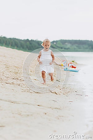 Cute baby girl runing and having fun on the beach near lake. The concept of summer holiday. baby`s day. Family spending Stock Photo