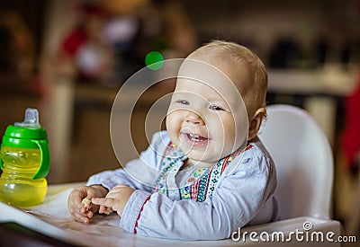 Cute baby girl sitting in high chair and eating piece of bread Stock Photo