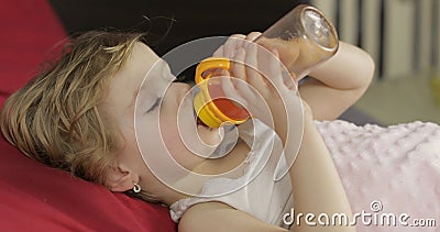 Cute baby girl sleeping on cozy bed at home and drinking juice from bottle Stock Photo