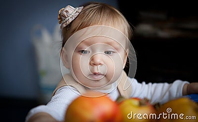 Cute baby looks on juicy red apples. Little girl reaching out for an apple Stock Photo