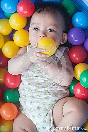 Cute baby lying in colorful toy balls and playing happily Stock Photo