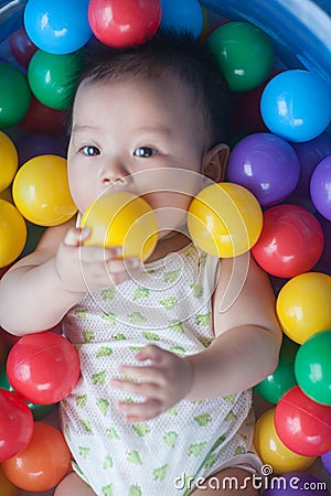 Cute baby lying in colorful toy balls and playing happily Stock Photo