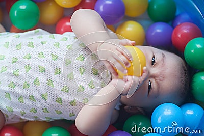 Cute baby lying in colorful toy balls and playing happily Stock Photo