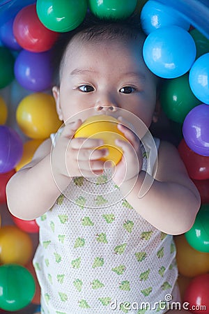 Cute baby lying in colorful toy balls and playing happily Stock Photo